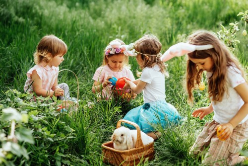 Ostereiersuche. Eine Gruppe von Kindern mit Hasenohren rennt los, um bei der Ostereiersuche im Garten bunte Eier aufzuheben. Ostertradition. Lachende Kinder im Park mit einem Korb – Frühlingsmotiv