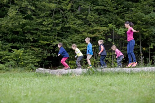 Kindergärtnerin spielt mit Kindern auf einem Baumstamm