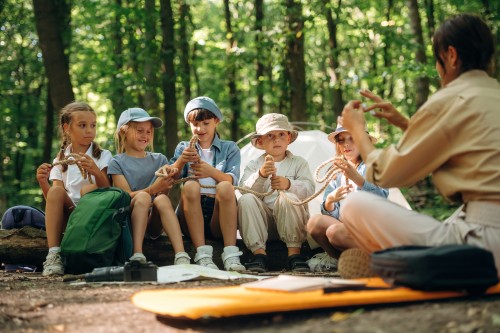 Überlebenstipps am Lagerfeuer. Eine Frau führt eine Gruppe von Kindern durch den Wald.